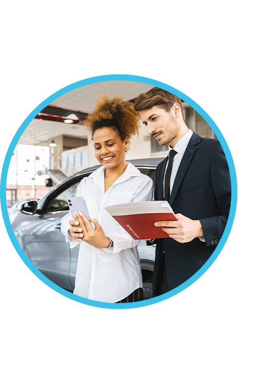 A car salesperson and vehicle owner smiling and looking at a phone together in the car dealership